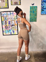 Load image into Gallery viewer, A woman stands in front of a wall wearing a beige athletic two-piece set consisting of a tank top and fitted shorts. prints.
