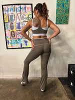 Load image into Gallery viewer, A woman stands on a runway wearing a matching beige athletic set consisting of a sports bra and flared leggings with white contrast trim. 
