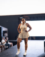 Load image into Gallery viewer, A model wearing a beige sleeveless halter top with a pleated skort with shorts underneath
